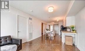 Toronto (Bayview Village) condo for rent - A living room with a black leather couch and a dining area with a white table and chairs.