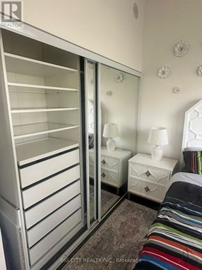 Toronto (Banbury-Don Mills) condo for rent - A white wardrobe with a mirror above it is in a room with a bed and two lamps.