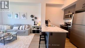 Hamilton (Waterdown) condo for rent - A modern kitchen with a breakfast bar and a living room area.
