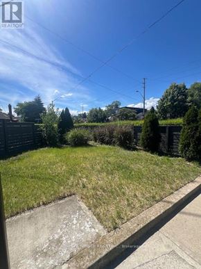 Toronto (East York) triplex for rent - A backyard with a grassy area and a concrete path.