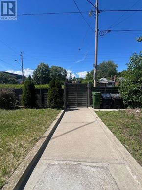 Toronto (East York) triplex for rent - A concrete pathway leads to a metal gate in a grassy area.