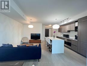 Toronto (Annex) condo for rent - A modern living room with a blue sofa and a kitchen area in the background.