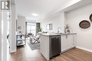Hamilton (Stoney Creek) condo for rent - A modern kitchen with a dining table and chairs in the foreground and a living room with a couch and a coffee table in the background.