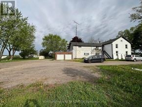 Cambridge apartment for rent - A gravel driveway leads to a white house with a black car parked in front.