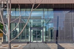 Toronto (South Parkdale) condo for rent - The image shows the front of a building with a glass door and a tree in front of it.