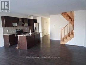 Hamilton (Stoney Creek) townhouse for rent - A spacious kitchen with dark wood floors and a staircase in the background.