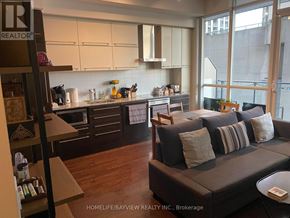 Toronto (Bay Street Corridor) condo for rent - A living room with a couch and a kitchen area in the background.