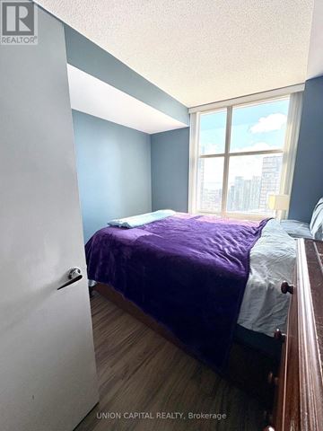 Toronto (Waterfront Communities) condo for rent - A bedroom with a purple bedspread and a window showing a cityscape.