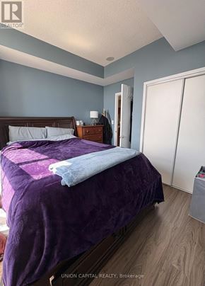 Toronto (Waterfront Communities) condo for rent - A bedroom with a purple bedspread and a wooden bed.