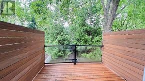 Toronto (Annex) townhouse for rent - A wooden deck with a glass railing overlooking a green forest.