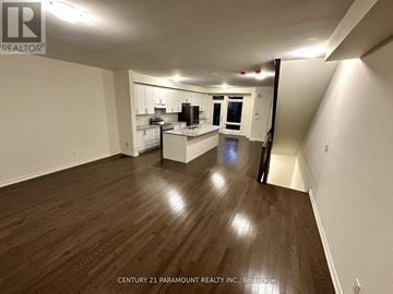 Ajax (South East) townhouse for rent - A spacious room with wooden flooring and white walls, featuring a kitchen area with white cabinets and appliances.