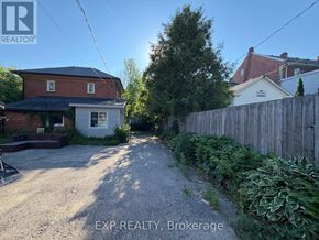 Orangeville multi-family for rent - A gravel driveway leads to a house with a white fence and green plants on the side.