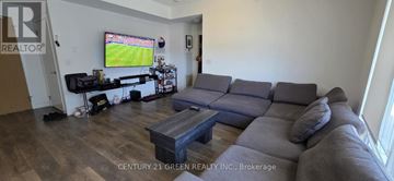 Mississauga (Central Erin Mills) condo for rent - A living room with a grey couch and a television showing a soccer game.