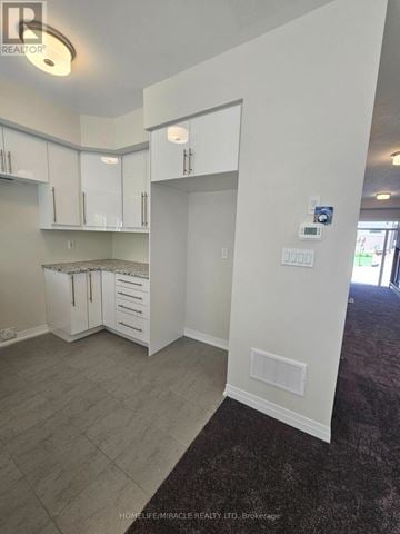 Brantford townhouse for rent - A real estate photo of a kitchen area with white cabinets and a grey floor.
