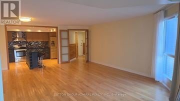 Richmond Hill (North Richvale) condo for rent - A spacious room with wooden flooring and a kitchen area with a stove and cabinets.