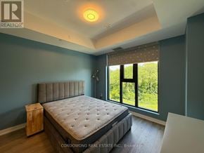 Toronto (Lawrence Park North) condo for rent - A bedroom with a large bed and a window overlooking a green landscape.