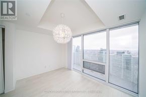 Toronto (Waterfront Communities) condo for rent - A large, empty room with a chandelier hanging from the ceiling and a view of the city through the windows.