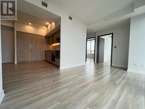 Toronto (Waterfront Communities) condo for rent - A spacious room with wooden flooring and a kitchen area in the background.