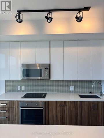 Ottawa condo for rent - A modern kitchen with white cabinets and a stainless steel microwave above the stove.