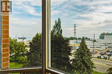 Burlington condo for rent - A view from a window looking out at a parking lot and a large building.