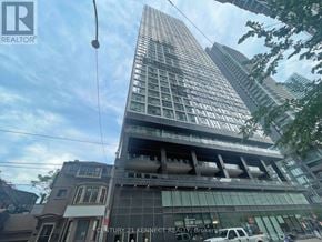 Toronto (Moss Park) condo for rent - A tall building with a glass facade stands in front of a tree.