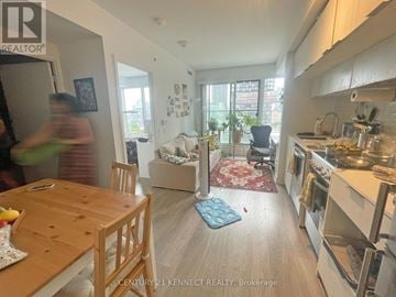 Toronto (Moss Park) condo for rent - A kitchen with a table and chairs in the foreground and a person walking in the background.