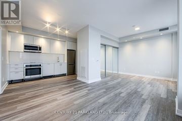 Toronto (High Park-Swansea) condo for rent - A spacious room with wood flooring and a kitchen area with white cabinets and appliances.
