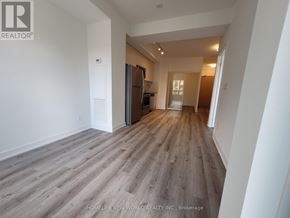 Toronto (Bayview Village) condo for rent - A spacious room with wooden flooring and white walls, with a kitchen area visible in the background.
