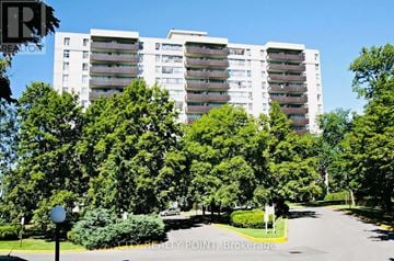 Toronto (Westminster-Branson) condo for rent - A large white building with balconies is surrounded by green trees.