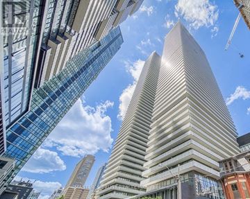 Toronto (Church-Yonge Corridor) condo for rent - A tall building with a pointed top is seen from a low angle, with other buildings and a blue sky in the background.