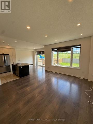 New Tecumseth (Tottenham) apartment for rent - A spacious room with wooden flooring and a kitchen area with a refrigerator and sink.