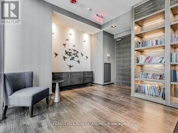Toronto (Bay Street Corridor) condo for rent - A living room with a grey chair and a bookshelf filled with books.