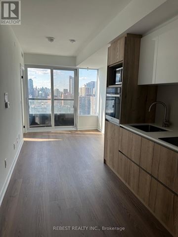Toronto (Moss Park) condo for rent - A kitchen with wooden floors and a large window overlooking a cityscape.