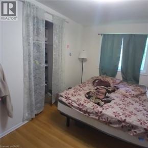 Kitchener apartment for rent - A bedroom with a bed, a lamp, and a window with curtains.