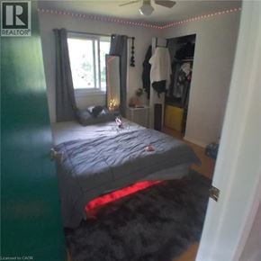 Kitchener apartment for rent - A bedroom with a bed, a window with curtains, a rug, a ceiling fan, and a coat hanging on the wall.