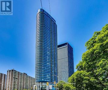 Toronto (North St. James Town) condo for rent - A tall blue glass building stands in front of a smaller building and trees.