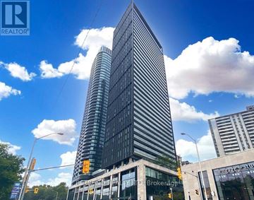 Toronto (North St. James Town) condo for rent - A tall building with a glass facade stands in front of a blue sky with clouds.