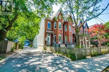 Toronto (Moss Park) triplex for rent - A red brick house with a white fence and trees in front.