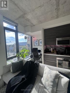 Toronto (Waterfront Communities) condo for rent - A living room with a couch, a plant, and a window overlooking a cityscape.