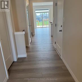 Tillsonburg townhouse for rent - A hallway with wooden floors and white walls leading to a doorway.