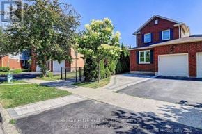 Oakville (Wc Wedgewood Creek) apartment for rent - A red brick house with a white garage door is surrounded by greenery.