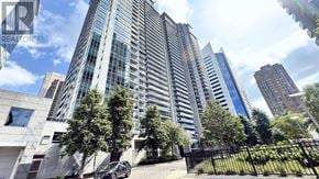 Toronto (Lansing-Westgate) condo for rent - A tall building with a glass facade stands in front of a tree.