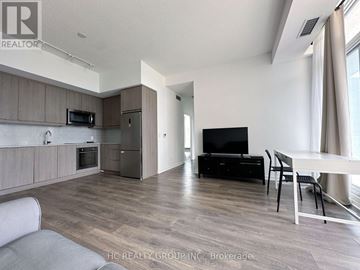 Toronto (Henry Farm) condo for rent - A modern living room with a grey sofa, a black TV, and a dining table with chairs.