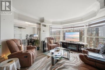 Mississauga (City Centre) condo for rent - A living room with brown leather furniture and a large window overlooking a cityscape.