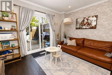 Toronto (Greenwood-Coxwell) townhouse for rent - A living room with a brown leather couch, a white coffee table, and a white brick wall with a painting hanging on it.