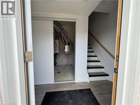 Welland townhouse for rent - A hallway with a staircase and a doorway leading to a room with a white wall and a black mat on the floor.