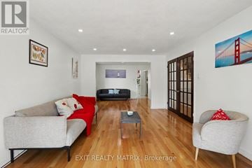 Ottawa apartment for rent - A living room with a grey couch, a red cushion, a black sofa, a grey armchair, a coffee table, and a painting of the Golden Gate Bridge on the wall.