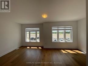 Barrie townhouse for rent - A room with wooden floors and two windows overlooking a parking lot.