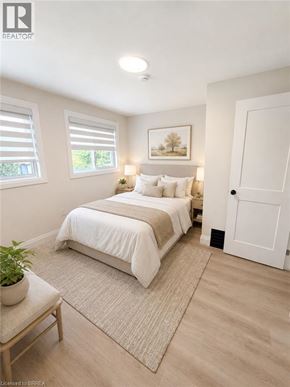 Hamilton apartment for rent - A bedroom with a bed, a nightstand, a window with blinds, a rug, a potted plant, and a painting on the wall.