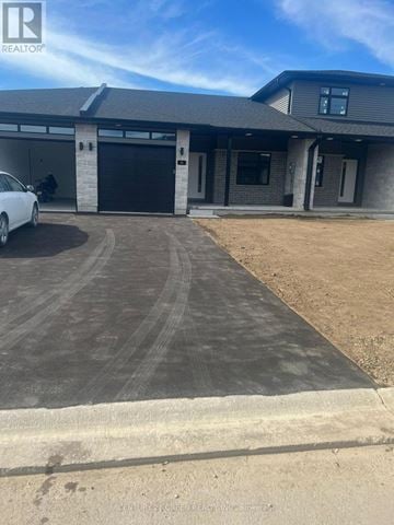 South Huron (Exeter) townhouse for rent - A white car is parked in front of a grey building with a black garage door.